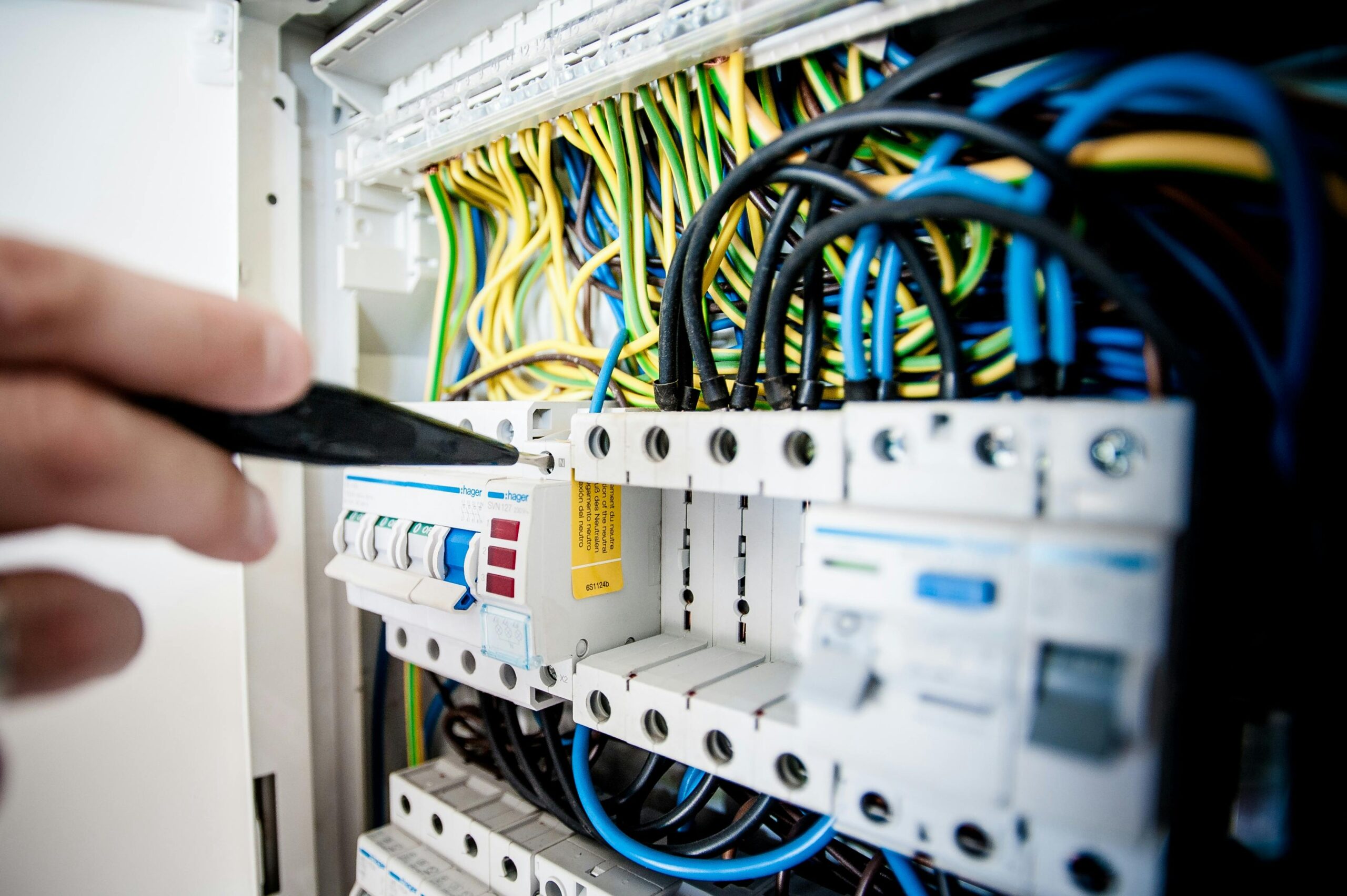 Soluciones Eléctricas Hand of electrician working on a circuit breaker panel with colorful wires, ensuring safe electrical connections.